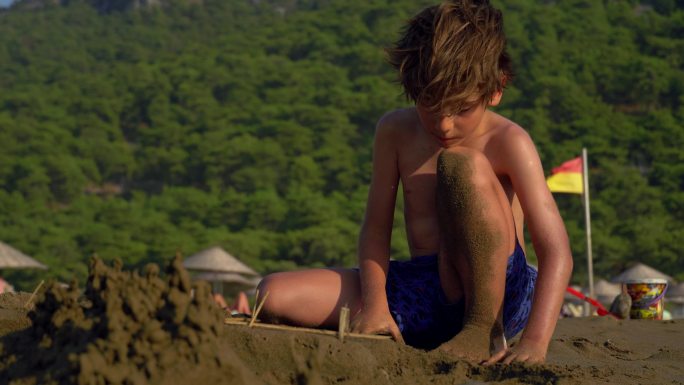 一个男孩在海滩上堆沙堡。