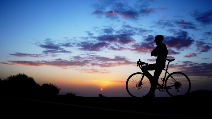 日落时岩石上自行车骑手的剪影。