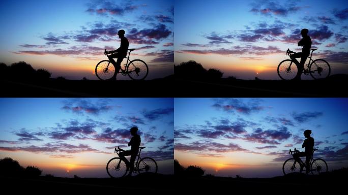 日落时岩石上自行车骑手的剪影。