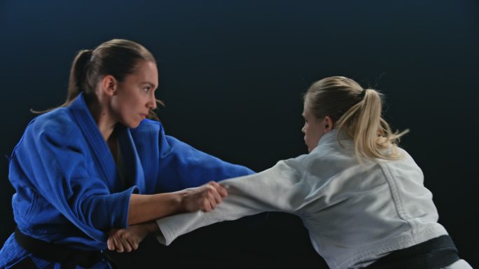两名女子柔道运动员在黑色背景下搏斗