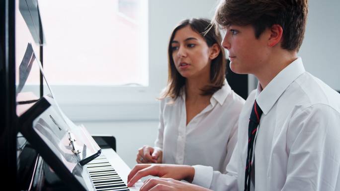 男学生和老师在音乐课上弹钢琴