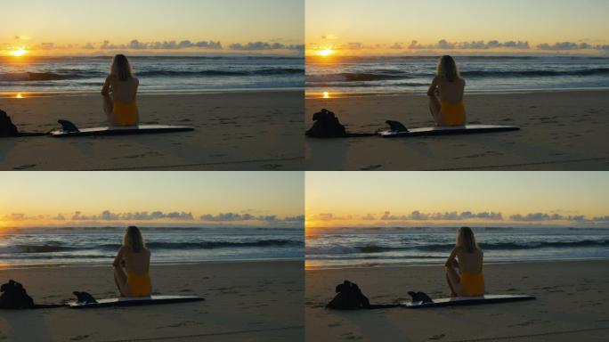 女子坐在沙滩的冲浪板上看日落