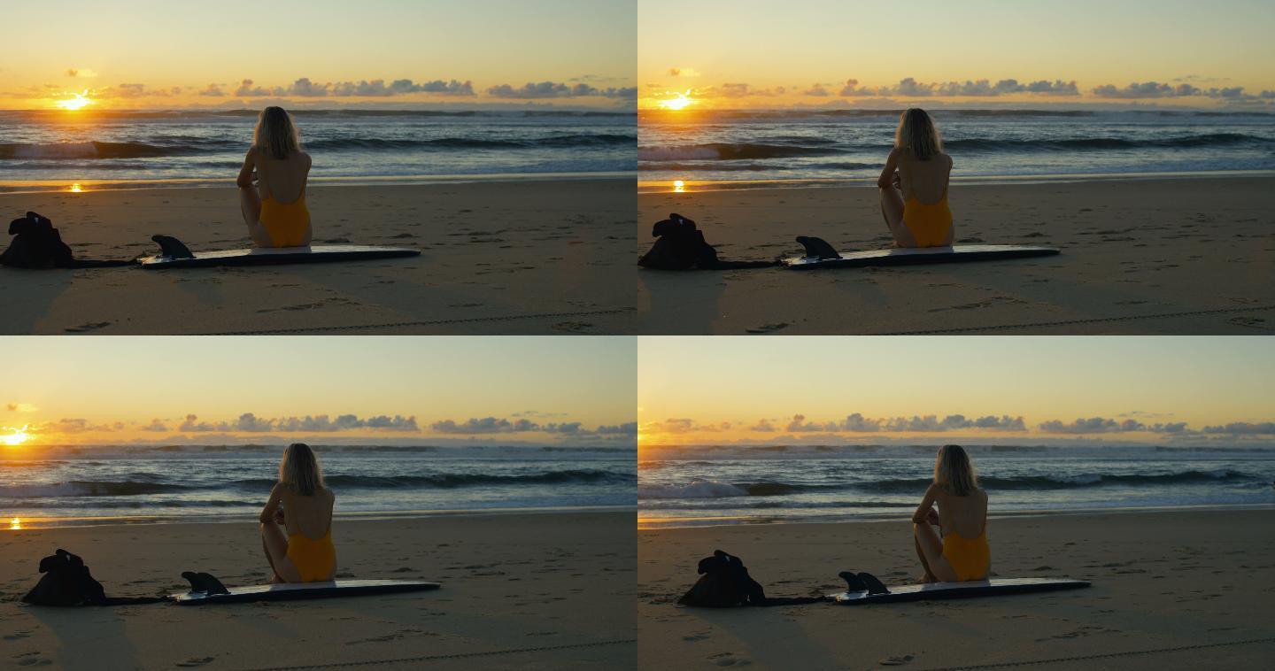女子坐在沙滩的冲浪板上看日落