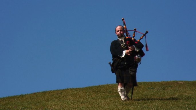身着传统苏格兰服装的风笛手在山顶上演奏