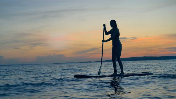 日落时女运动员在冲浪板上划船