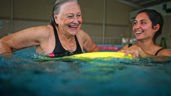 快乐的女性和游泳教练在泳池上课