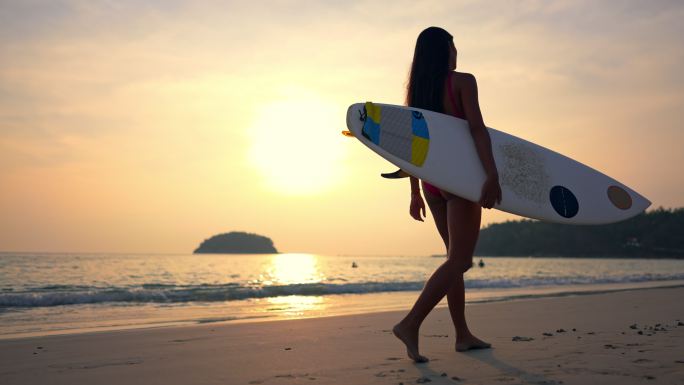女子手持冲浪板日落时在海滩上散步