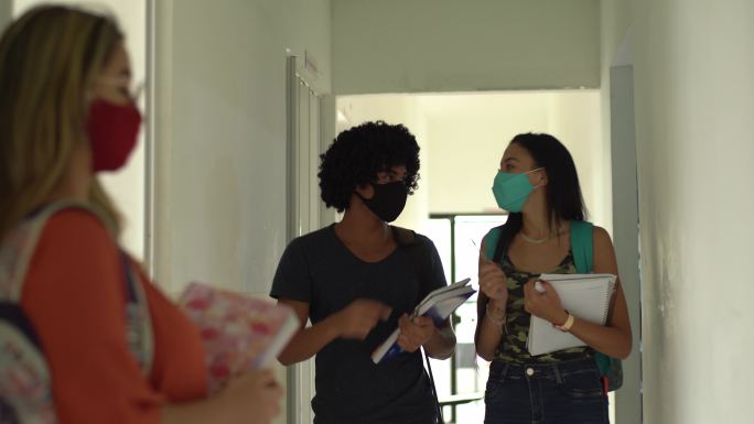 在大学走廊里，朋友们戴着口罩用肘部打招呼
