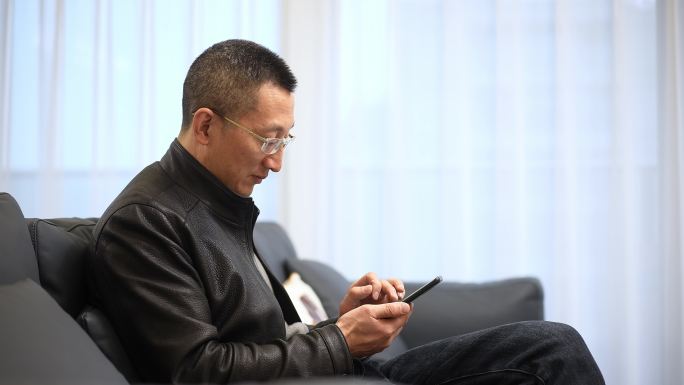 中年男子坐在客厅沙发上使用智能手机