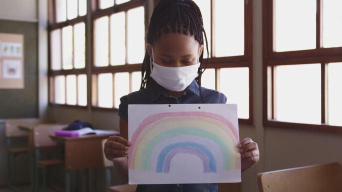 在学校的课堂上，戴着口罩拿着彩虹画的女孩