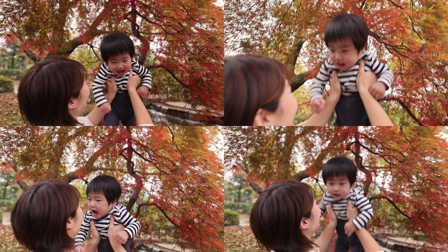 年轻的母亲在秋天的红叶下抱着她的小男孩