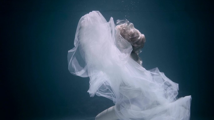穿着白色优雅连衣裙在水下游泳的美女