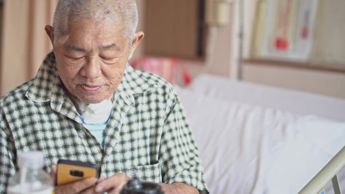 老年男性患者坐在病床上看着智能手机