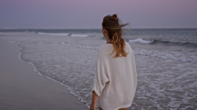 日落时独自在海滩上散步的女人