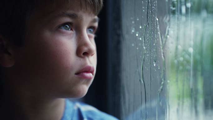 一个悲伤的小男孩在家透过窗户看雨