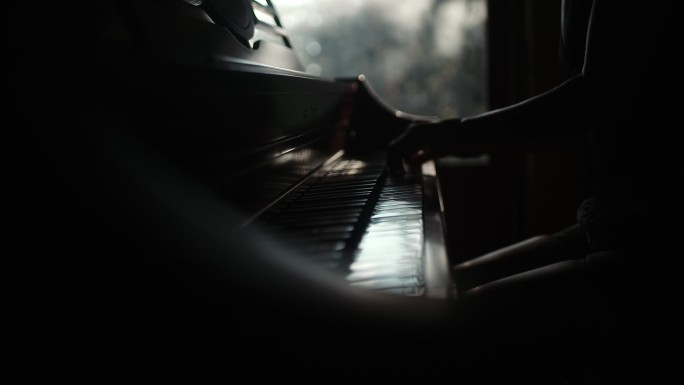 女性在黑暗房间的窗户旁轻轻地弹钢琴