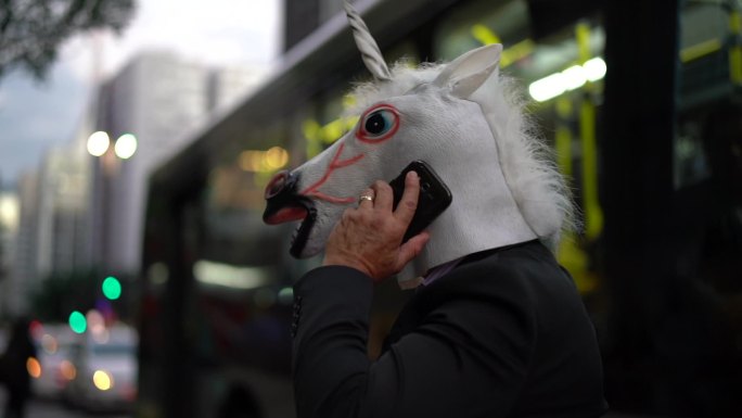戴着独角兽面具的商人在城市用手机聊天