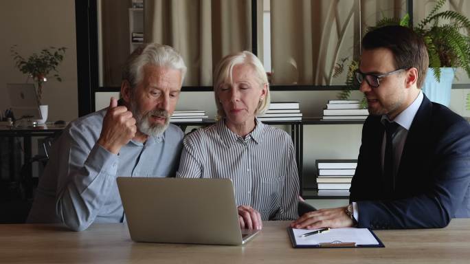 房地产经纪人在笔记本电脑上向老年客户介绍