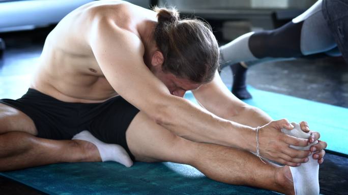 一名运动员坐在健身馆的地板上，伸展腿部