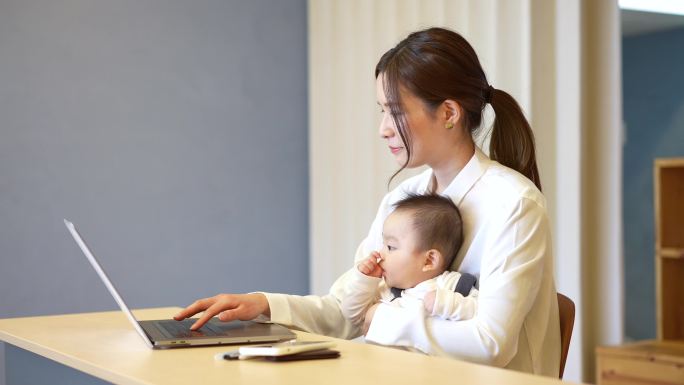 一个抱着婴儿操作笔记本电脑的女人