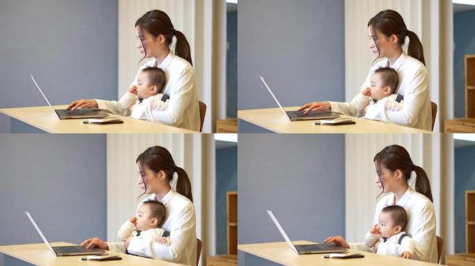 一个抱着婴儿操作笔记本电脑的女人