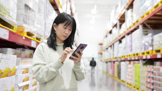 年轻女性在现代超市里使用智能手机购物