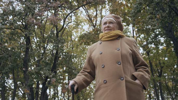 老年妇女拄着拐杖在秋季公园散步