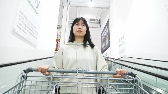 年轻女性自动扶梯上推着超市购物车逛商超