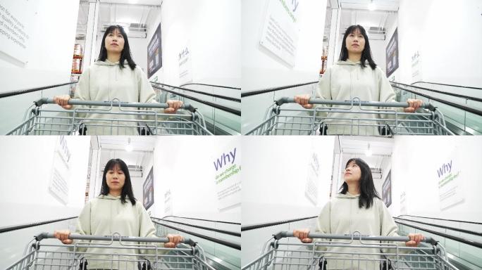 年轻女性自动扶梯上推着超市购物车逛商超