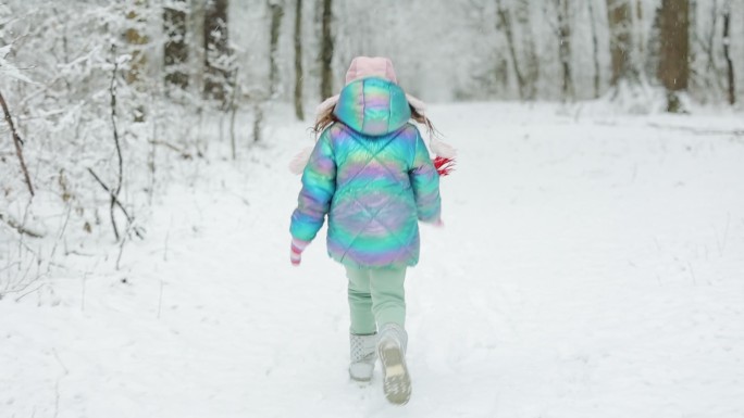 小女孩在冰雪覆盖的冬季公园里奔跑