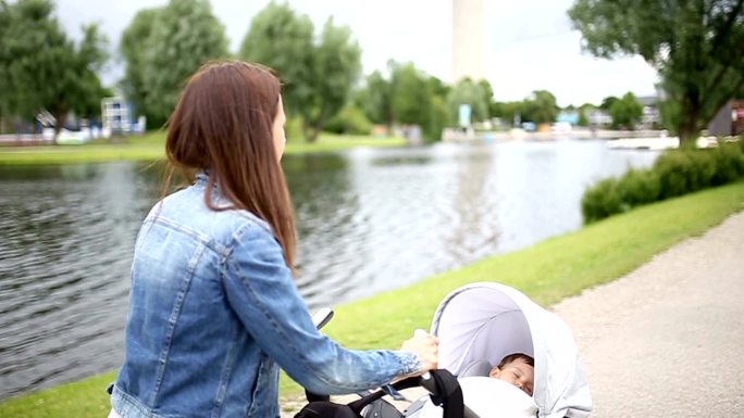 快乐的妈妈和推着婴儿在公园散步。