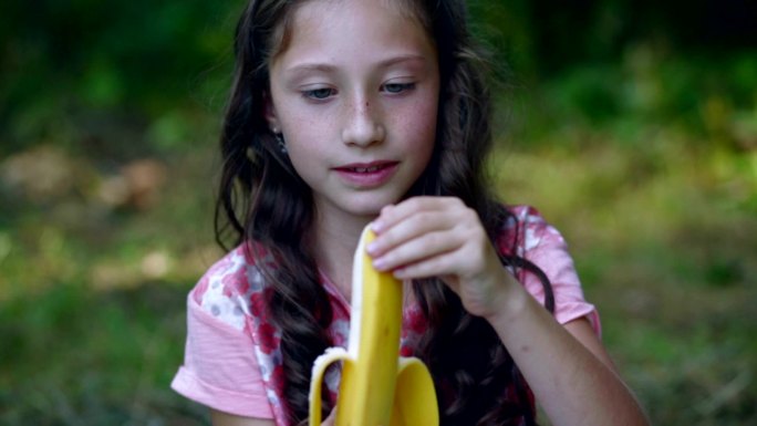美丽的小女孩在花园里吃香蕉