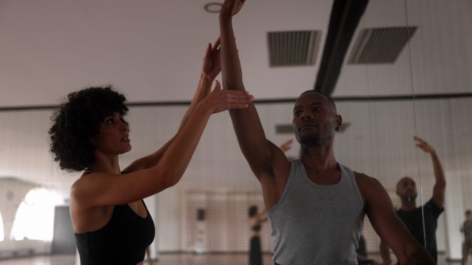 教练在舞蹈室调整男舞者的手臂姿势