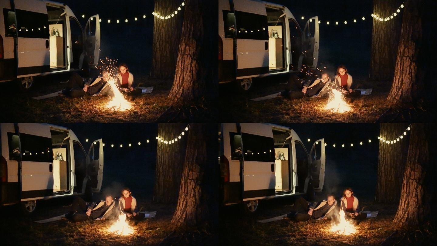 男女坐在篝火旁野营夫妻情侣房车自驾游