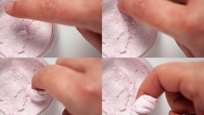 女人用手指从罐子里取出粉色的身体乳