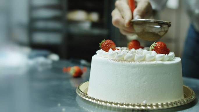 用草莓和糖霜装饰蛋糕的面包师