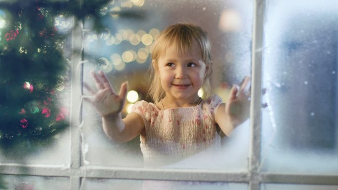 在平安夜，可爱的小女孩透过窗户微笑着。