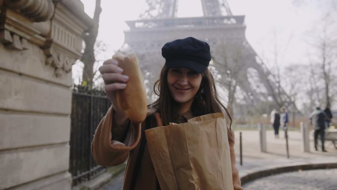 女人走在埃菲尔铁塔附近吃面包。