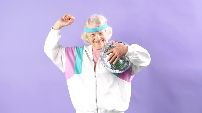 快乐微笑的老妇人穿着运动服，举着镜子球