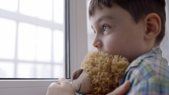 抱着玩具泰迪熊的小孩，看着窗外