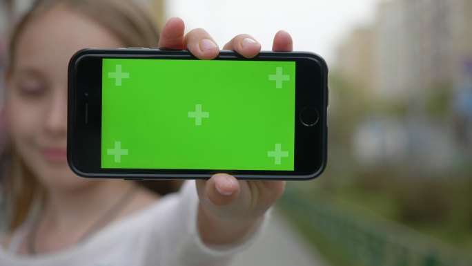 女孩向摄像机展示了一部带有绿色屏幕的手机