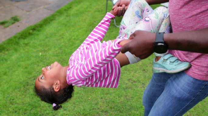 一个小女孩在户外玩耍时爬上她的父亲