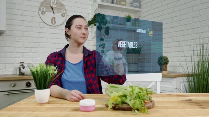 厨房里的美女使用虚拟屏幕在网上购买蔬菜