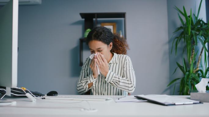 一名女商人坐在办公桌前打喷嚏