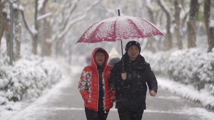 雪地里夫妻打伞有说有笑的走路