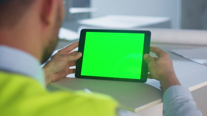 工程师手持带有绿色屏幕的平板电脑。
