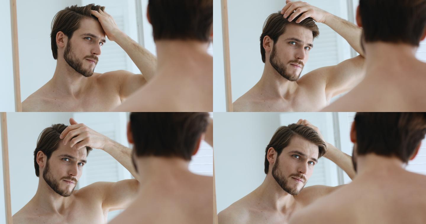 男子看着镜子，用手指梳理发型