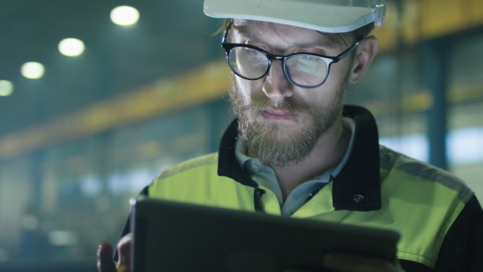 安全帽工程师正在一家工厂使用平板电脑。