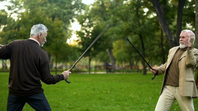 有趣的男性朋友在公园里用拐杖击剑