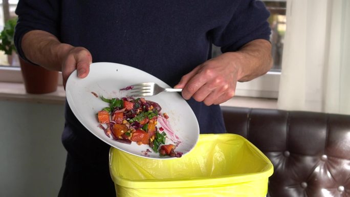 一个男人把盘子里没吃的食物扔进垃圾箱